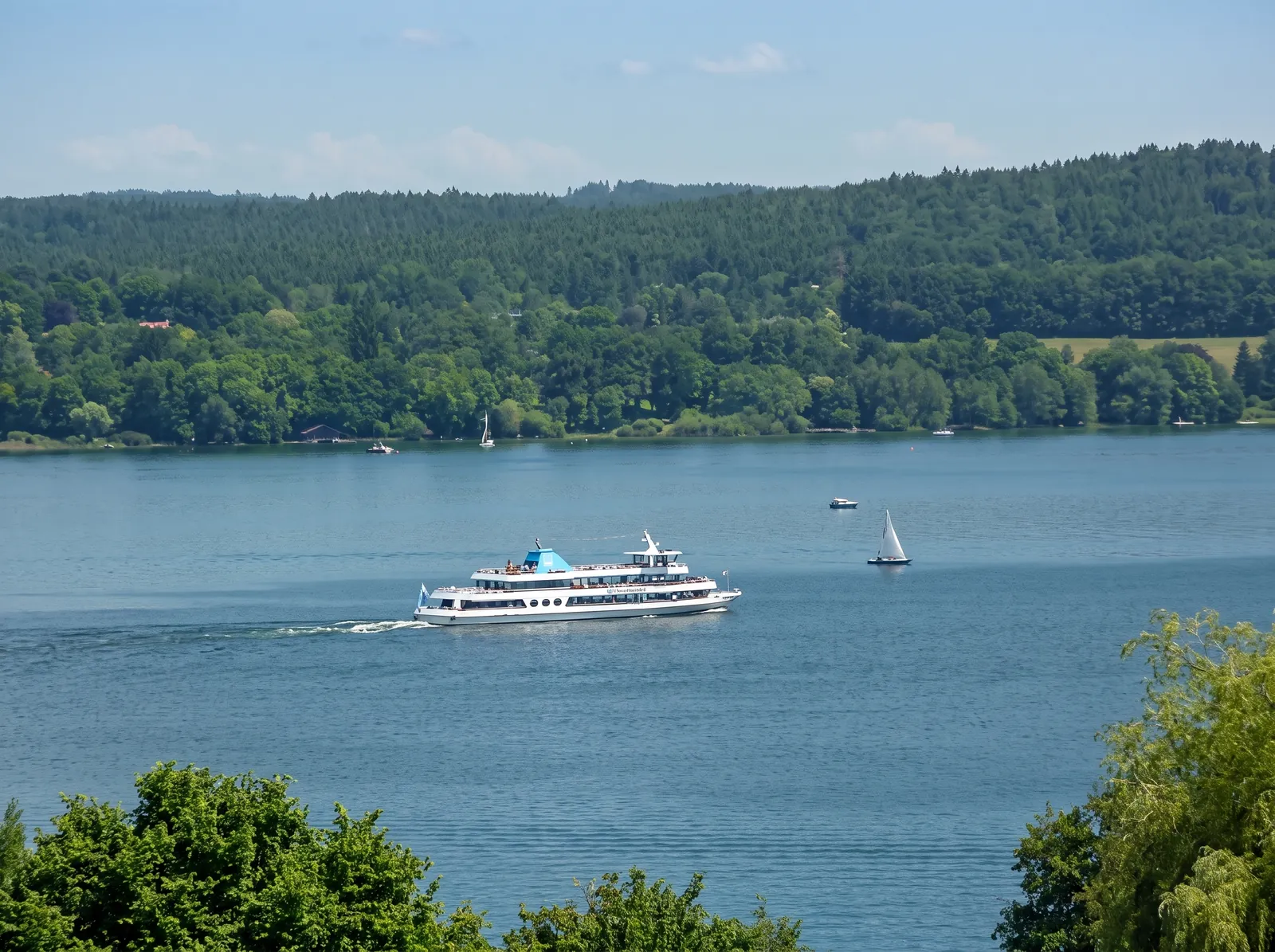 Weites Seepanorama mit Ausflugsschiff und bewaldetem Ufer