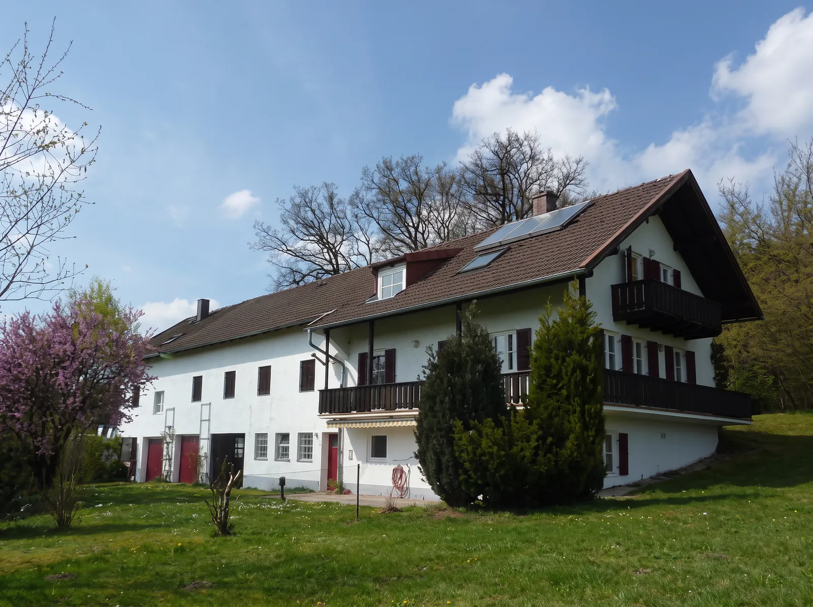 Langgestreckter bayerischer Bauernhof mit weißer Fassade und roten Fensterläden