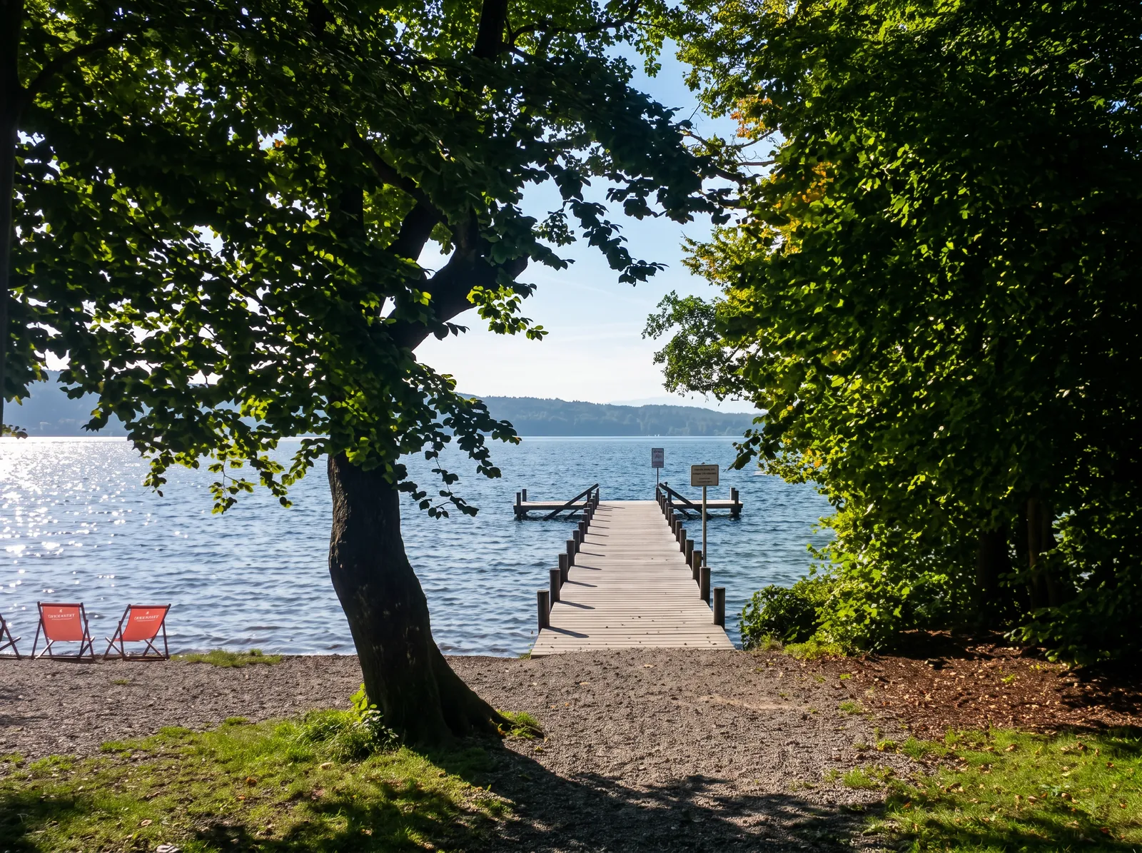 Hölzerner Bootssteg, der zwischen alten Bäumen in den Starnberger See führt